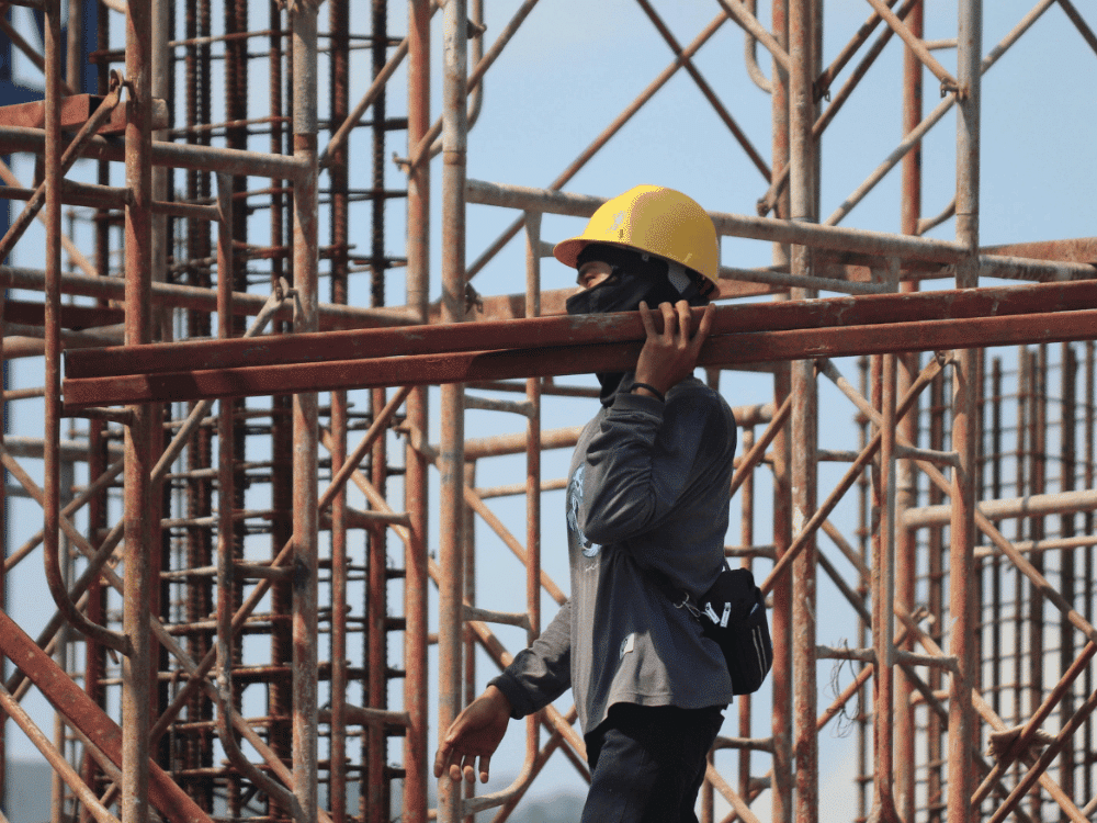Construction worker in a yellow helmet inspecting scaffolding.