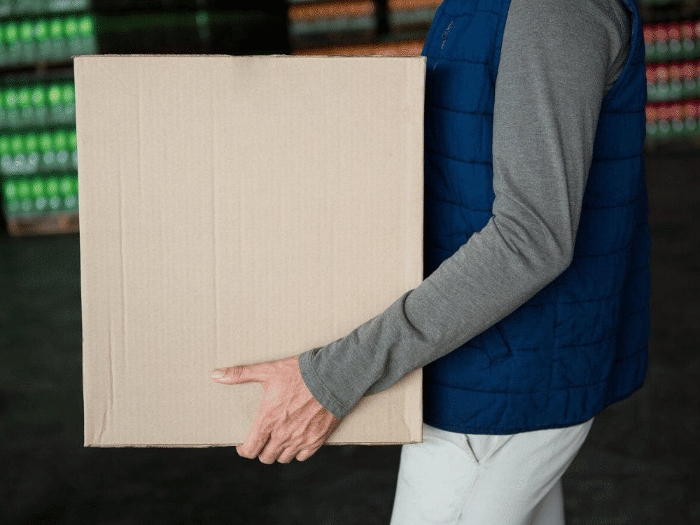 A person holding a cardboard box in a warehouse.
