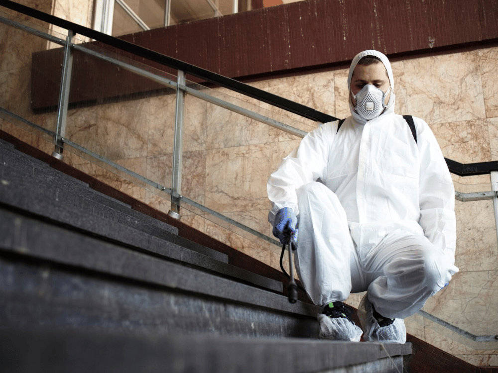 Professional in protective hazmat suit with respirator sitting on stairs.