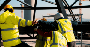 Construction workers in high-visibility jackets assemble a steel structure on a clear day.