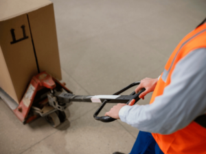 Close-up of a warehouse employee operating a hand pallet truck with a large box.