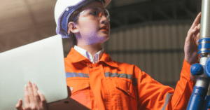 A woman in an orange safety suit holding a laptop, ready for work in a hazardous environment.