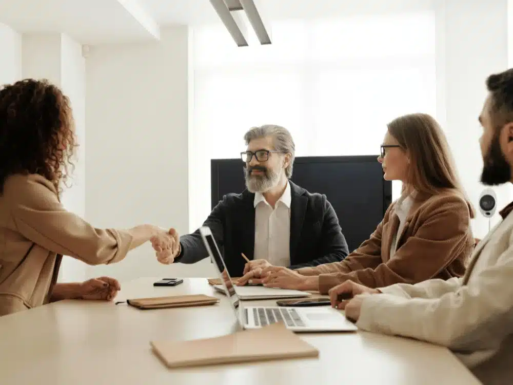 Colleagues shaking hands during a business meeting with two others observing.