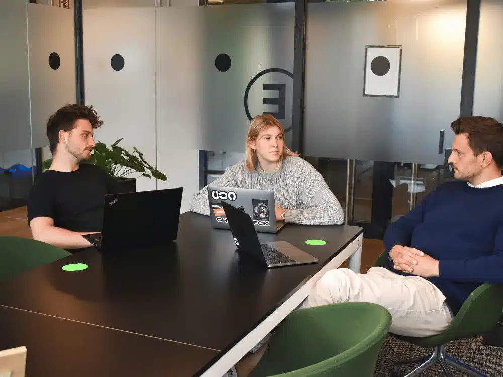 Team members engaged in a serious discussion around laptops in a modern office.