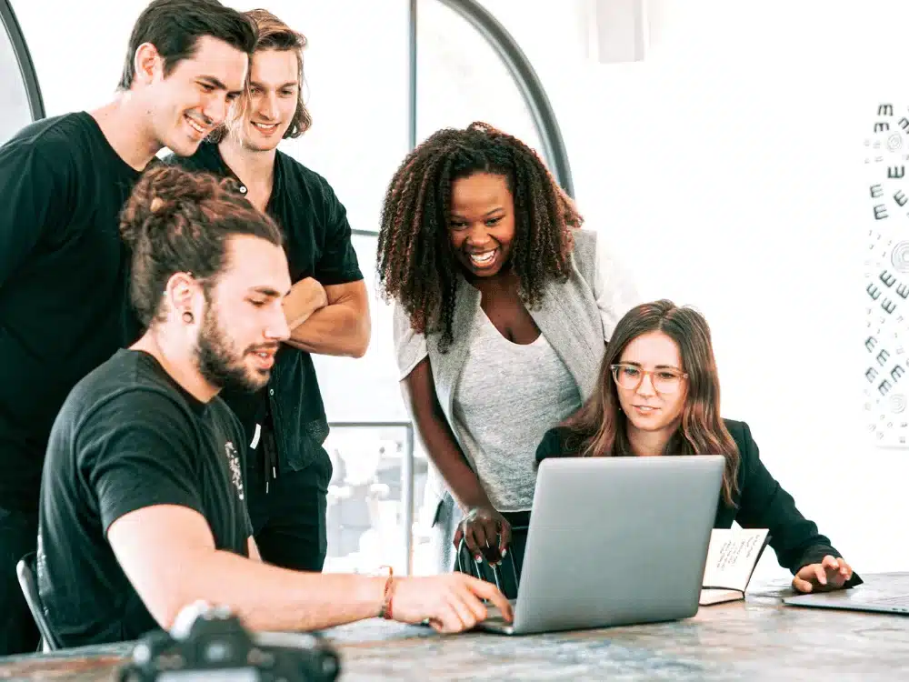 Diverse team of coworkers smiling and discussing a project on a laptop.
