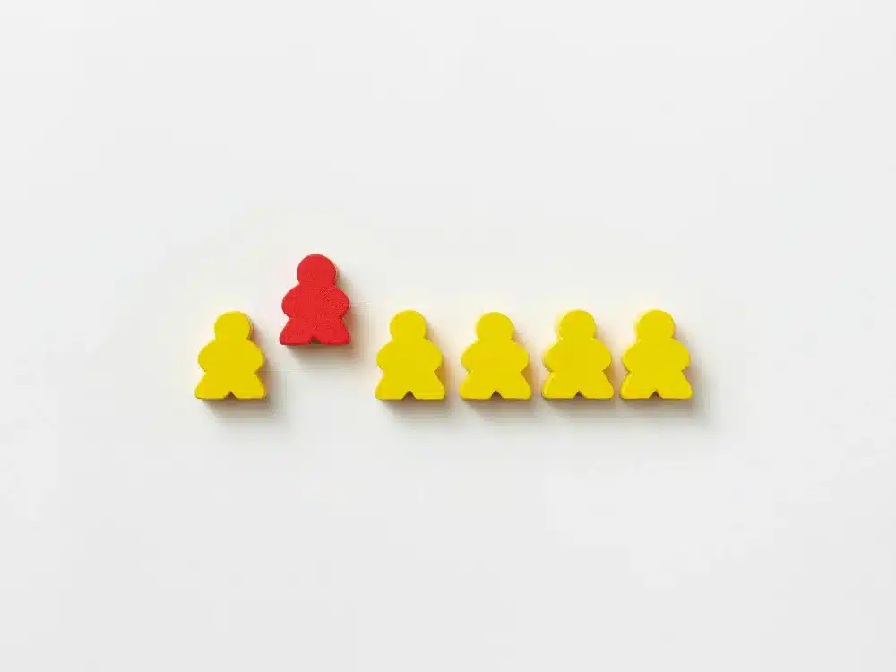 Red figurine standing out among yellow figures symbolizing leadership or uniqueness.