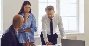 A group of professionals engaged in discussion at a bright, modern office, with documents and a computer on the table.