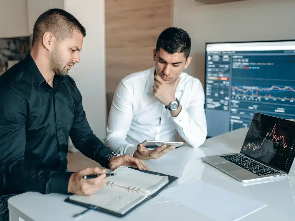 Two businessmen analyzing stock market data on screens.