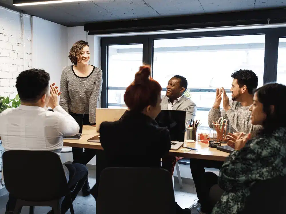 Woman being applauded by team during office meeting.